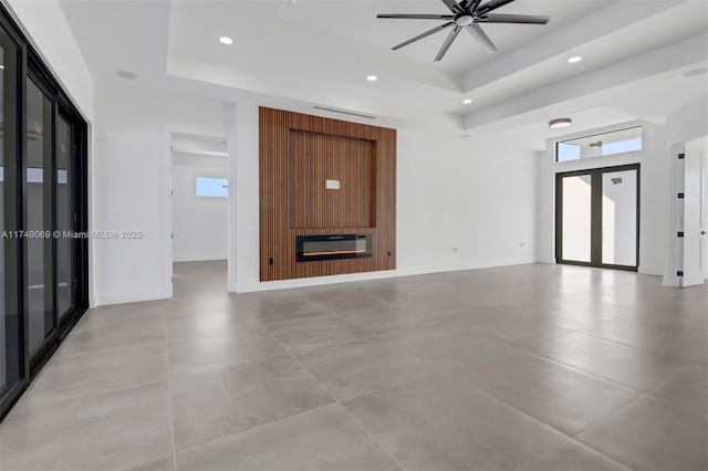 unfurnished living room with recessed lighting, a raised ceiling, a fireplace, and baseboards