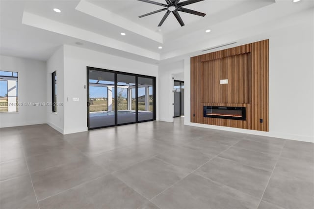 unfurnished living room with baseboards, a raised ceiling, ceiling fan, a fireplace, and recessed lighting