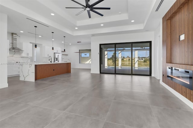 unfurnished living room with a ceiling fan, a tray ceiling, a sink, and recessed lighting