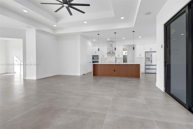 unfurnished living room featuring baseboards, a raised ceiling, ceiling fan, a sink, and recessed lighting