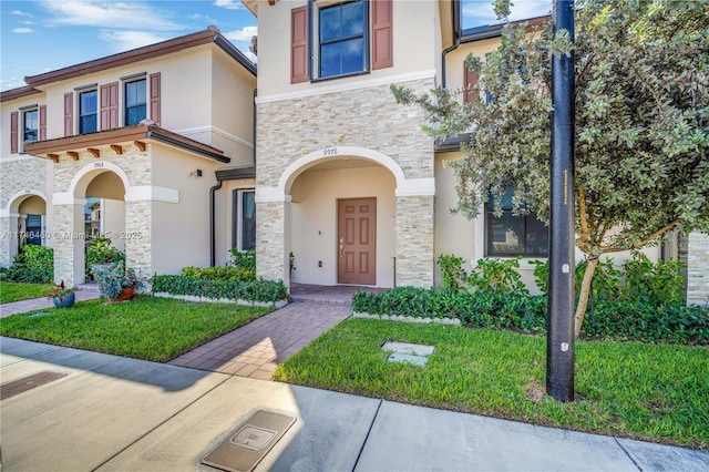 view of front of property with stone siding, a front lawn, and stucco siding