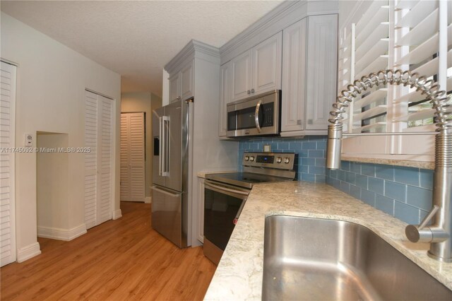 8639 Eagle Run Dr Unit 11, Boca Raton, FL 33434 - kitchen featuring appliances with stainless steel finishes, light wood finished floors, backsplash, baseboards, and light stone counters