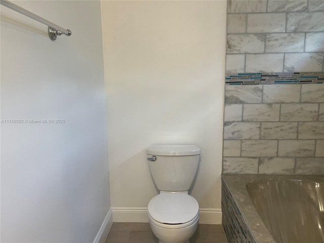 bathroom featuring a washtub, baseboards, and toilet