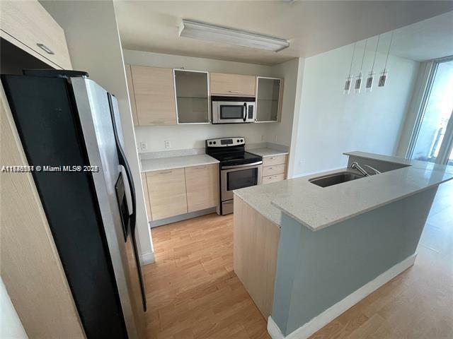 kitchen with a center island with sink, light hardwood / wood-style flooring, light stone countertops, sink, and appliances with stainless steel finishes