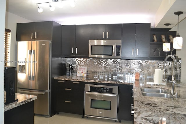 kitchen with sink, light stone counters, pendant lighting, stainless steel appliances, and decorative backsplash