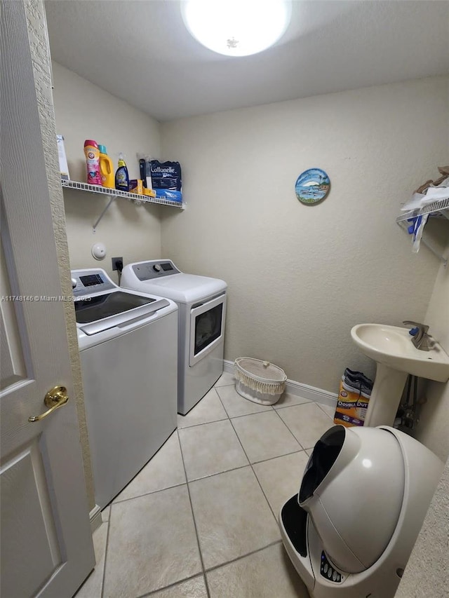 clothes washing area with sink, light tile patterned floors, and independent washer and dryer