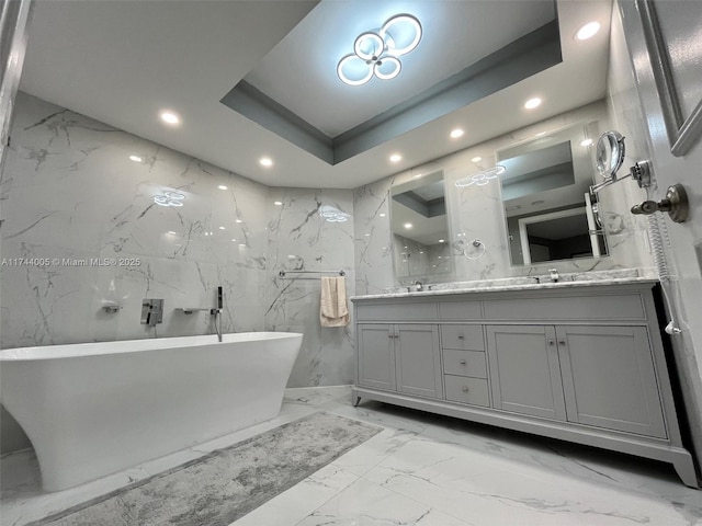 bathroom featuring a tray ceiling, vanity, tile walls, and a bath