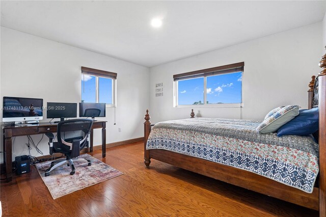 bedroom with multiple windows, baseboards, and wood finished floors