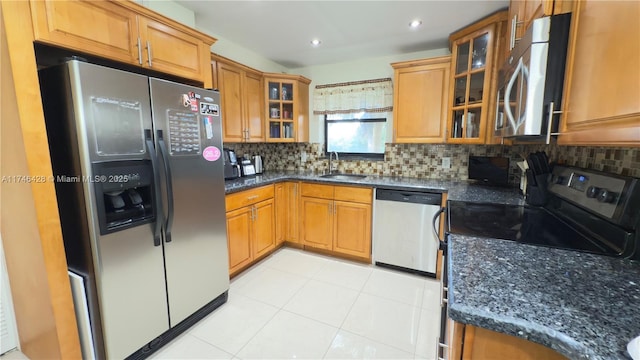 kitchen featuring backsplash, dark stone counters, brown cabinetry, stainless steel appliances, and a sink
