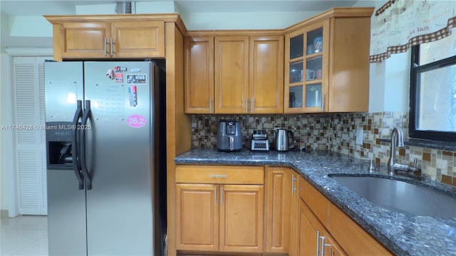 kitchen featuring a sink, dark stone counters, backsplash, and stainless steel fridge with ice dispenser