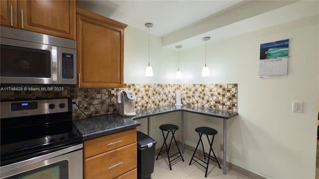 kitchen featuring light tile patterned floors, stainless steel appliances, decorative backsplash, decorative light fixtures, and brown cabinets