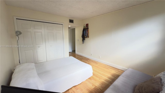 bedroom featuring visible vents, baseboards, light wood-type flooring, a closet, and a textured ceiling