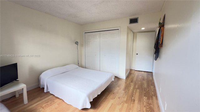 bedroom with light wood-type flooring, visible vents, a textured ceiling, and a closet