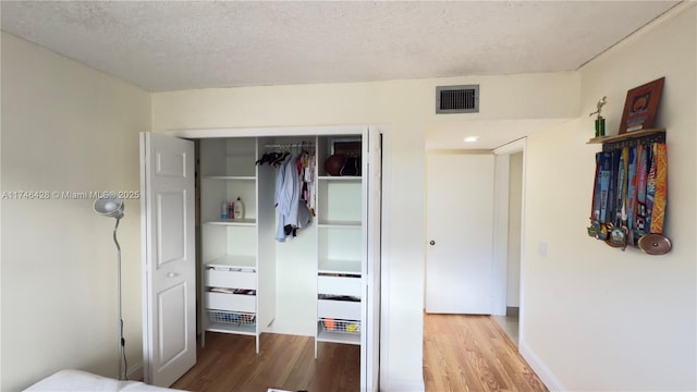 unfurnished bedroom with visible vents, a textured ceiling, and wood finished floors