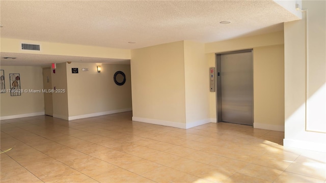 spare room with elevator, visible vents, a textured ceiling, and baseboards