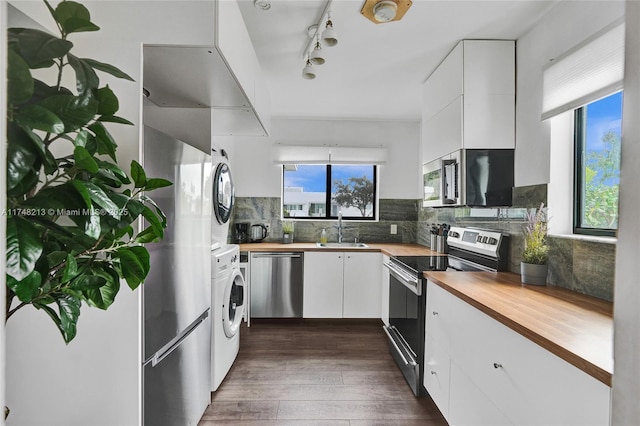 kitchen featuring wooden counters, stainless steel appliances, white cabinets, stacked washer / drying machine, and sink