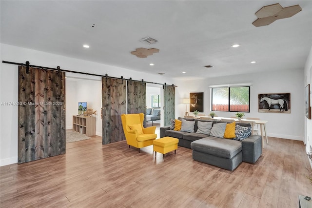 living room with light wood-type flooring, a barn door, and a healthy amount of sunlight