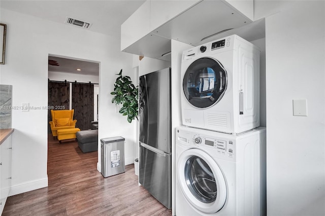 laundry room with hardwood / wood-style floors, stacked washer and dryer, and a barn door