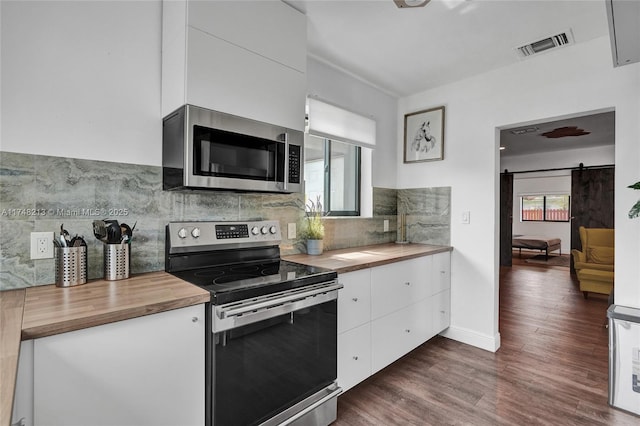 kitchen featuring white cabinetry, stainless steel appliances, a barn door, tasteful backsplash, and dark wood-type flooring