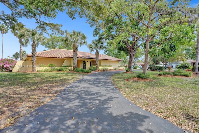 mediterranean / spanish-style house featuring aphalt driveway, stucco siding, a tile roof, and a front yard