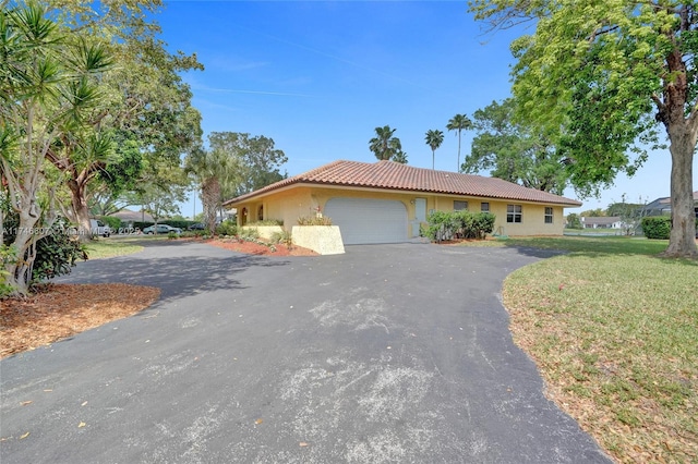 single story home featuring stucco siding, a tile roof, aphalt driveway, a front yard, and an attached garage