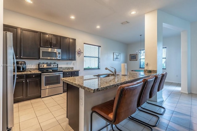 kitchen with hanging light fixtures, stainless steel appliances, sink, dark stone counters, and a kitchen breakfast bar