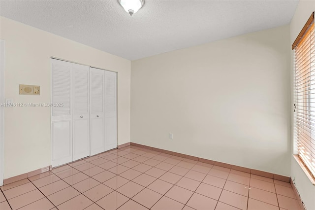 unfurnished bedroom featuring a closet, a textured ceiling, baseboards, and light tile patterned floors