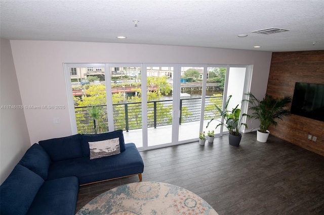 living area featuring a textured ceiling, recessed lighting, wooden walls, visible vents, and dark wood finished floors