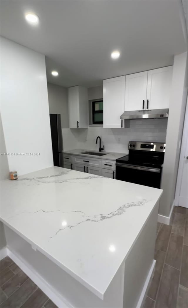 kitchen with white cabinetry, kitchen peninsula, sink, light stone counters, and appliances with stainless steel finishes