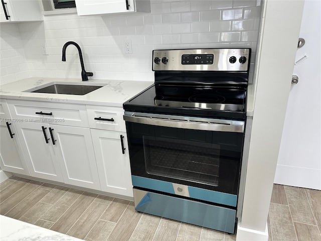 kitchen with sink, stainless steel range with electric cooktop, white cabinetry, and light stone countertops