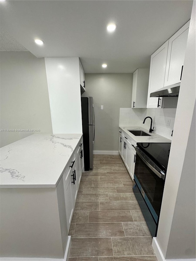 kitchen with sink, light stone counters, black electric range, stainless steel fridge, and white cabinets