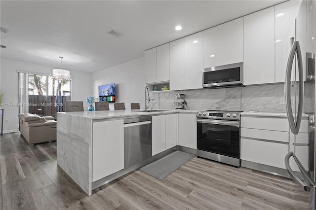 kitchen with appliances with stainless steel finishes, light hardwood / wood-style flooring, backsplash, white cabinetry, and hanging light fixtures