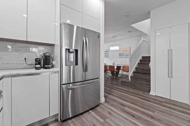kitchen with decorative light fixtures, stainless steel refrigerator with ice dispenser, hardwood / wood-style floors, backsplash, and white cabinets