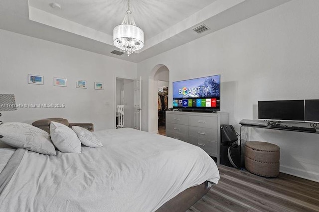 bedroom featuring a tray ceiling, dark hardwood / wood-style flooring, a walk in closet, and a notable chandelier