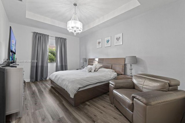 bedroom with a tray ceiling, hardwood / wood-style floors, and a notable chandelier