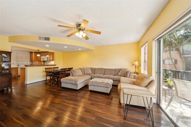 living room featuring ceiling fan, dark wood-type flooring, and a textured ceiling