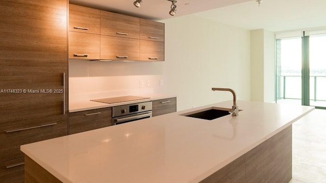 kitchen with sink, a kitchen island with sink, stainless steel oven, and rail lighting