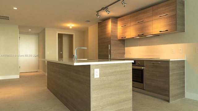 kitchen featuring an island with sink, sink, oven, and light tile patterned floors