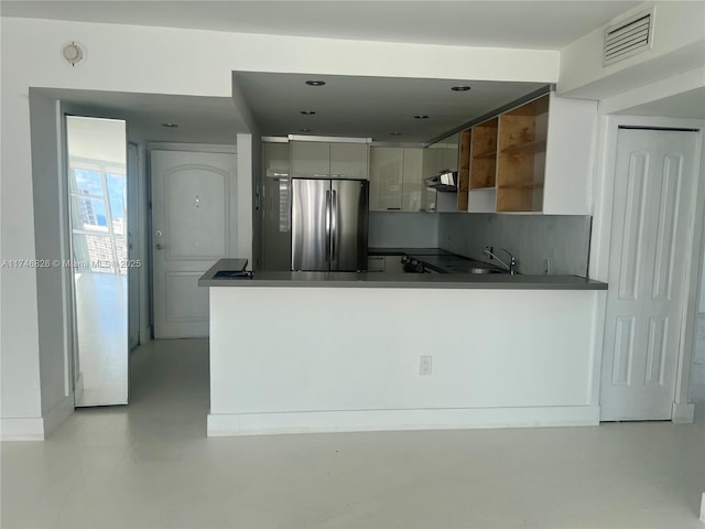 kitchen with sink, kitchen peninsula, white cabinets, and stainless steel fridge