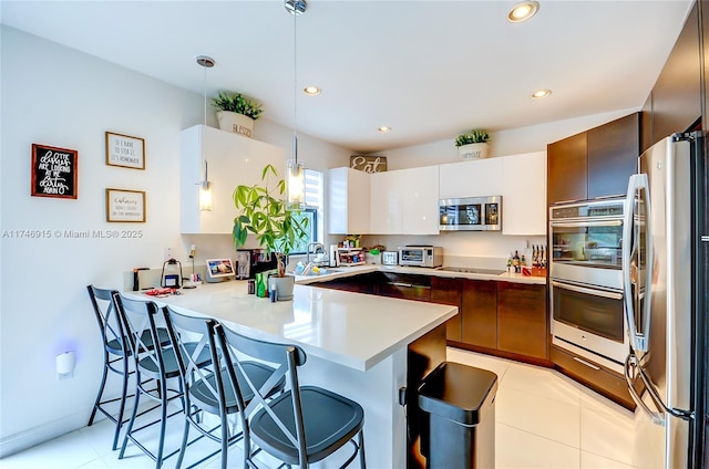 kitchen featuring appliances with stainless steel finishes, a breakfast bar, pendant lighting, kitchen peninsula, and white cabinets