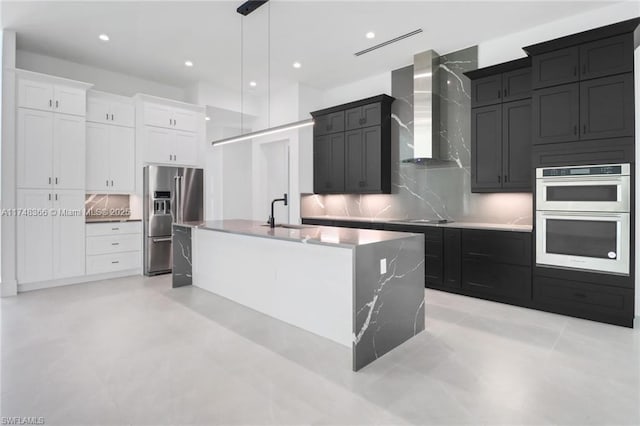 kitchen with white cabinetry, a kitchen island with sink, sink, appliances with stainless steel finishes, and wall chimney exhaust hood