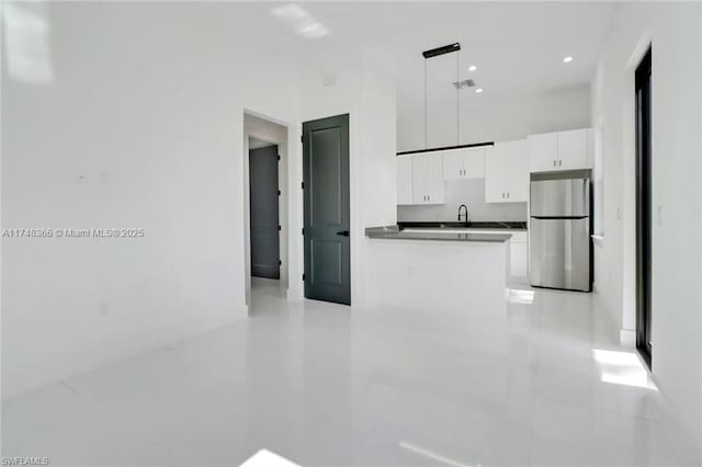 kitchen featuring hanging light fixtures, stainless steel refrigerator, and white cabinets