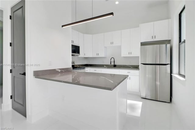 kitchen with stainless steel appliances, dark stone counters, sink, white cabinetry, and kitchen peninsula