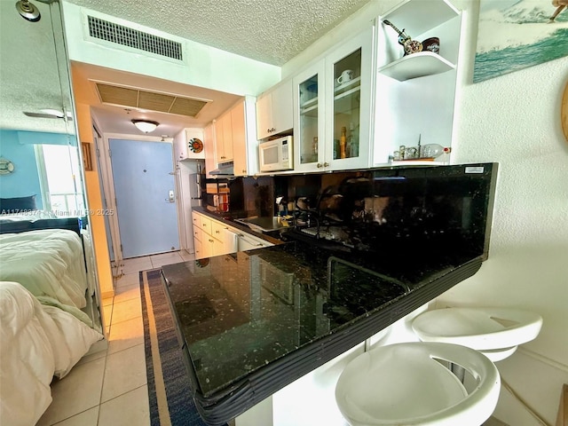 kitchen featuring a kitchen bar, light tile patterned floors, a textured ceiling, kitchen peninsula, and white cabinets