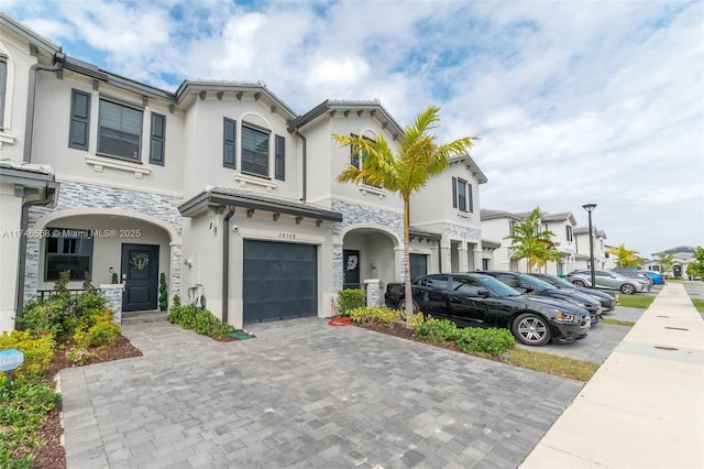 mediterranean / spanish-style house with an attached garage, stone siding, decorative driveway, and stucco siding