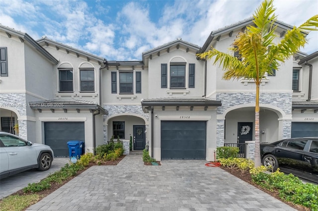 townhome / multi-family property with an attached garage, stone siding, decorative driveway, and stucco siding