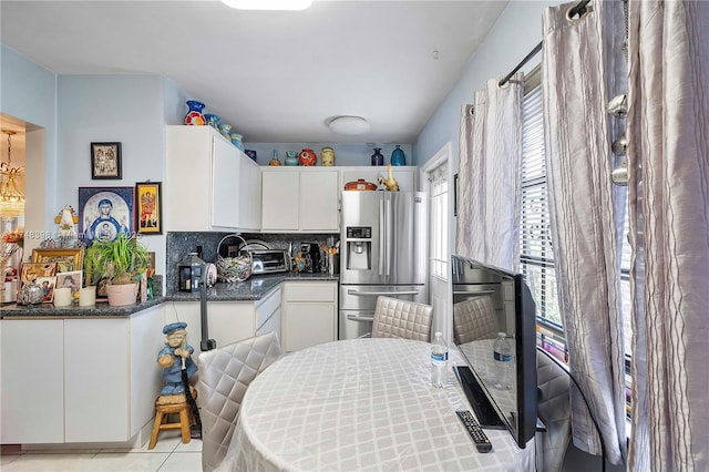 kitchen featuring light tile patterned floors, tasteful backsplash, stainless steel fridge, a toaster, and white cabinets