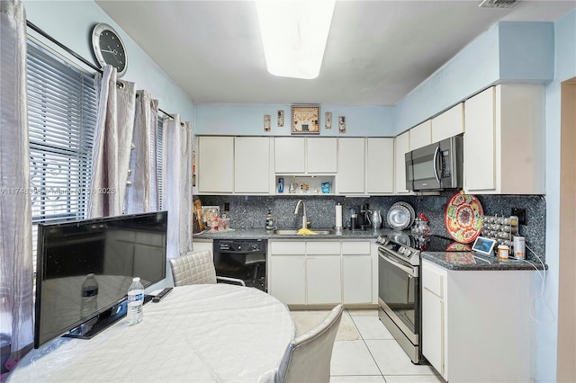kitchen with stainless steel appliances, dark countertops, a sink, and white cabinetry
