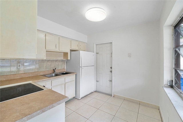 kitchen with a sink, light countertops, freestanding refrigerator, tasteful backsplash, and cooktop