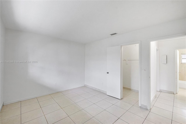 unfurnished bedroom featuring light tile patterned floors, baseboards, visible vents, a walk in closet, and a closet